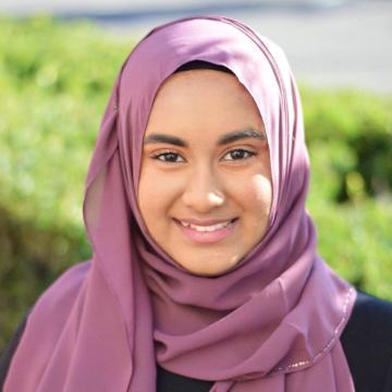 A person wearing a pink headscarf, smiling outdoors.