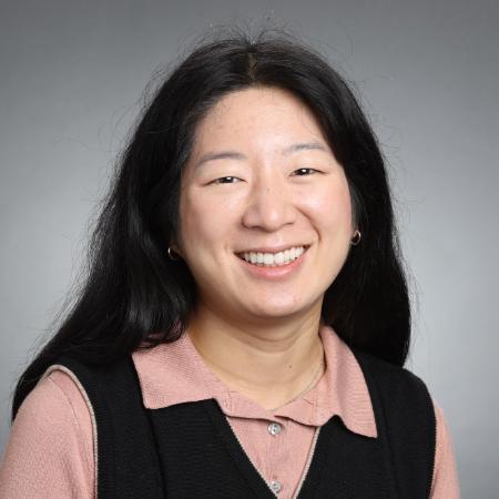 A person smiling in front of a gray background.
