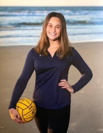 A woman holding a yellow water polo ball, standing on a beach.