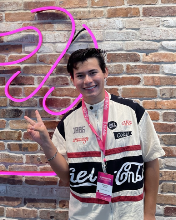 Person posing with peace sign in front of brick wall with neon lights.