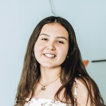 Smiling person wearing a necklace and patterned top with a light blue background.