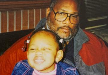 A man and a young girl smiling together indoors.