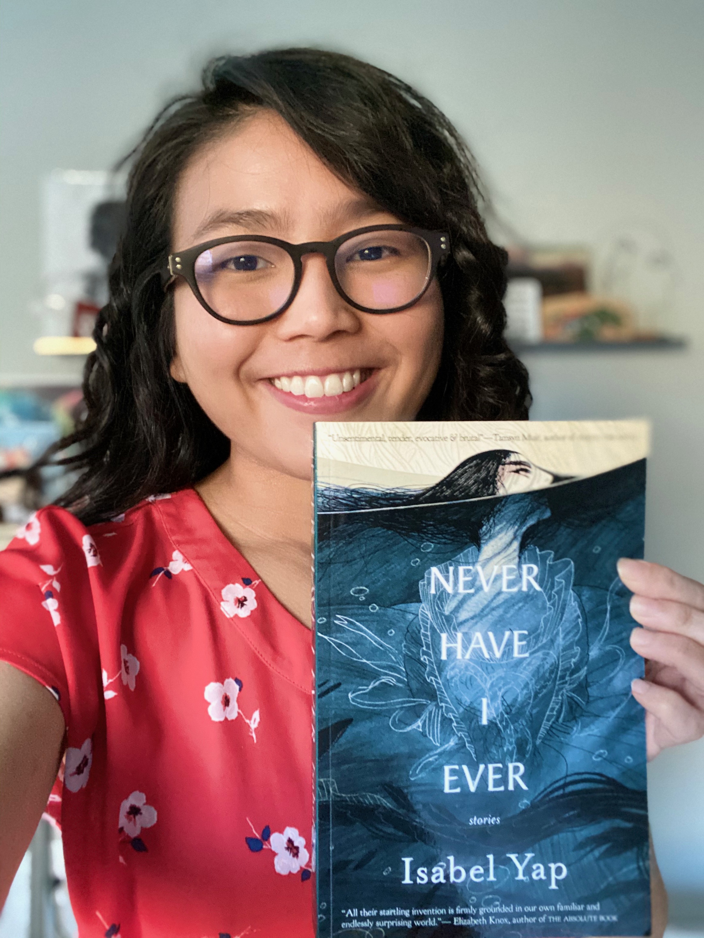 A person holding up a book titled "Never Have I Ever" by Isabel Yap.
