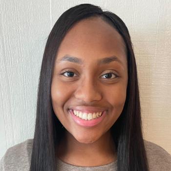 Smiling individual with long hair standing against a white background.