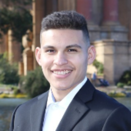 A person in a suit standing in front of a lake.