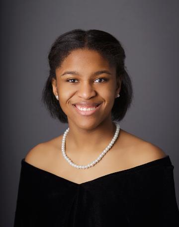 A person smiling in formal attire with a pearl necklace.