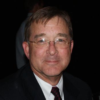 A person dressed formally smiling against a dark background.