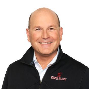 A man smiling, wearing a black zip-up jacket with 