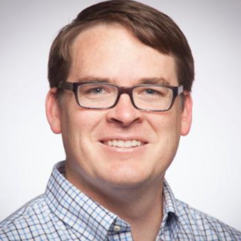 A person wearing glasses and a checkered shirt, smiling.