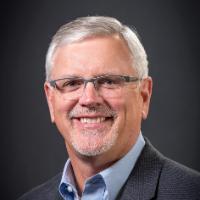 A man with glasses smiling, with the title "Drew Starbird".