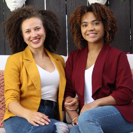 Two people seated on a couch, smiling, wearing yellow and red blazers.