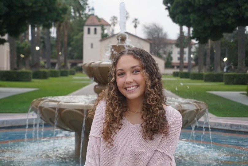 A person smiling in front of a fountain and building.