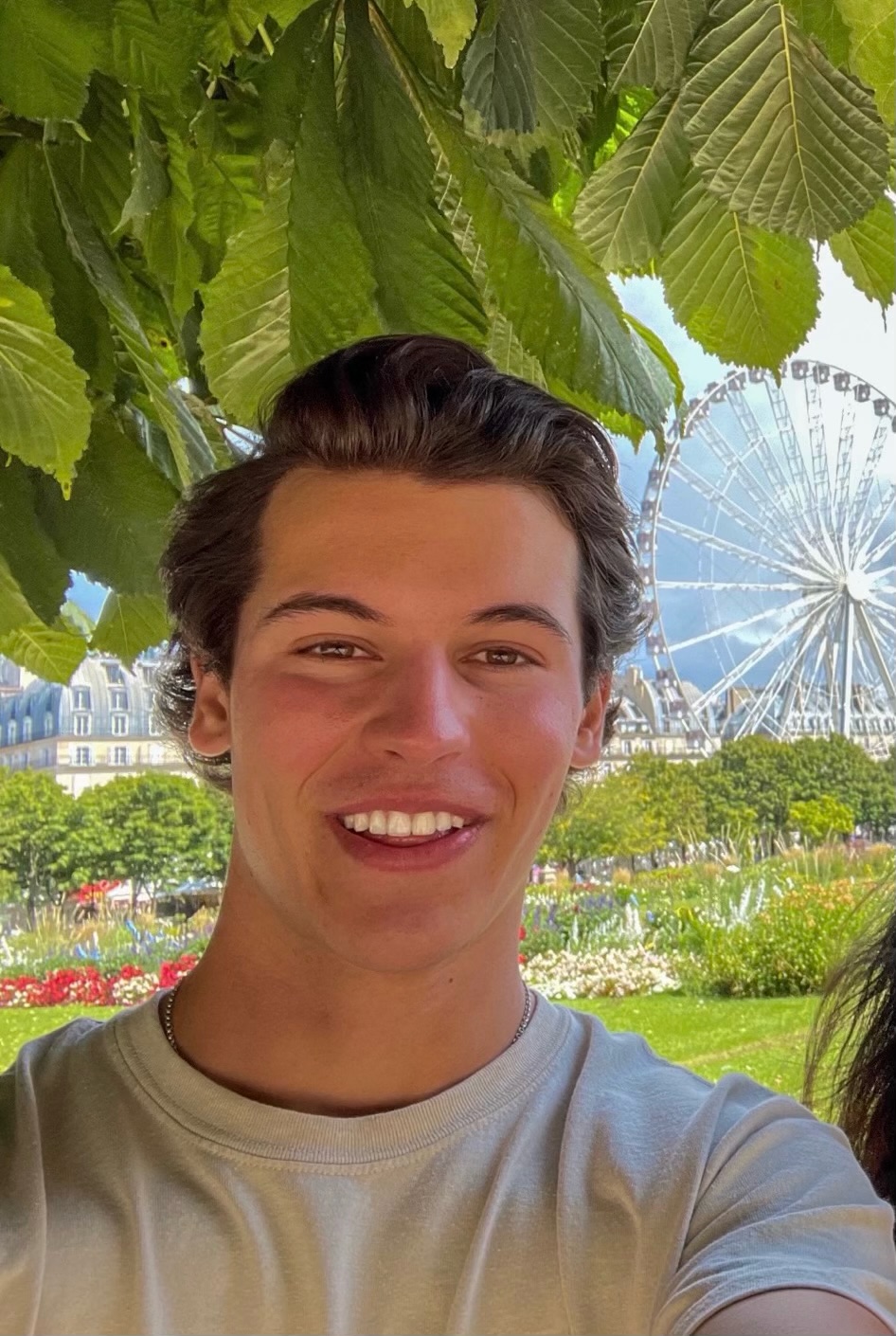 A person smiling outdoors with trees and sky in the background.