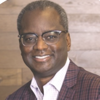 A person in a purple blazer smiling. Image titled 'Derrick Roman'.