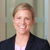 A person smiling, wearing a black jacket and light-colored top.