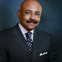 A man in a suit and tie smiling against a dark background.