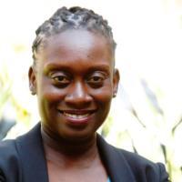 A person in a black jacket and blue top smiling.