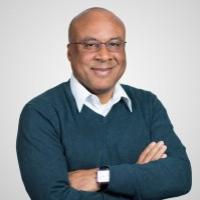 A smiling person in glasses and a teal sweater with folded arms.