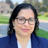 A person wearing glasses, smiling, in an outdoor setting.