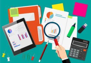 A desk with business documents, graphs, calculator, tablet, and magnifying glass.