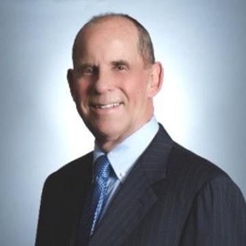 A man in a suit smiling against a plain background.