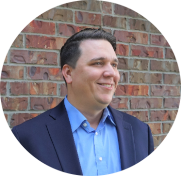Man in a suit smiling in front of a brick wall.