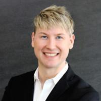 Man in a suit smiling against a dark background.