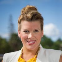 A person wearing a yellow necklace, white vest, and black top, outdoors.