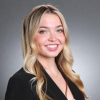 A woman with a smile, dressed in business attire against a gray background.