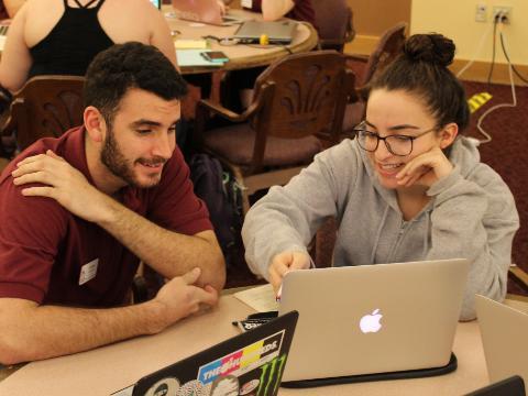 Two people sitting at a table working on a laptop. image link to story