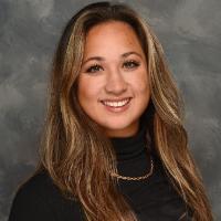 A person smiling in front of a grey background.