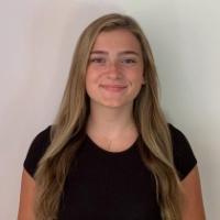 A person in a black shirt standing against a white wall.