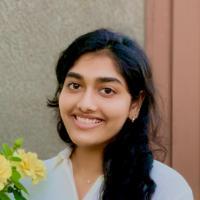 A person smiling next to yellow flowers.