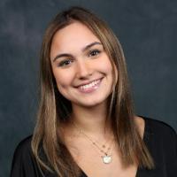 A person smiling against a dark studio background.
