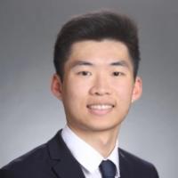 A person wearing a suit and tie against a grey background.
