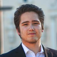A person in a suit standing outdoors with buildings in the background.