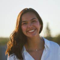 A person smiling outdoors with trees in the background.