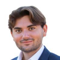A man in a suit smiling against a white background.