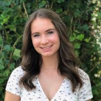 A woman in a white dress standing in front of greenery.