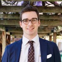 A person in a suit standing in a garden setting.