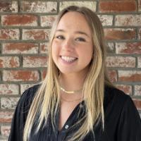 A person smiling in front of a brick wall.