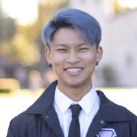 A person smiling outdoors in formal attire.