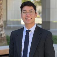 A person in a suit stands outdoors smiling.