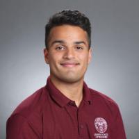 A person in a maroon shirt with a logo stands smiling.