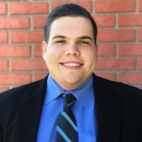 Smiling man in business attire standing against a brick wall.