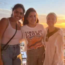 Three people posed together with a cityscape and sunset in the background.