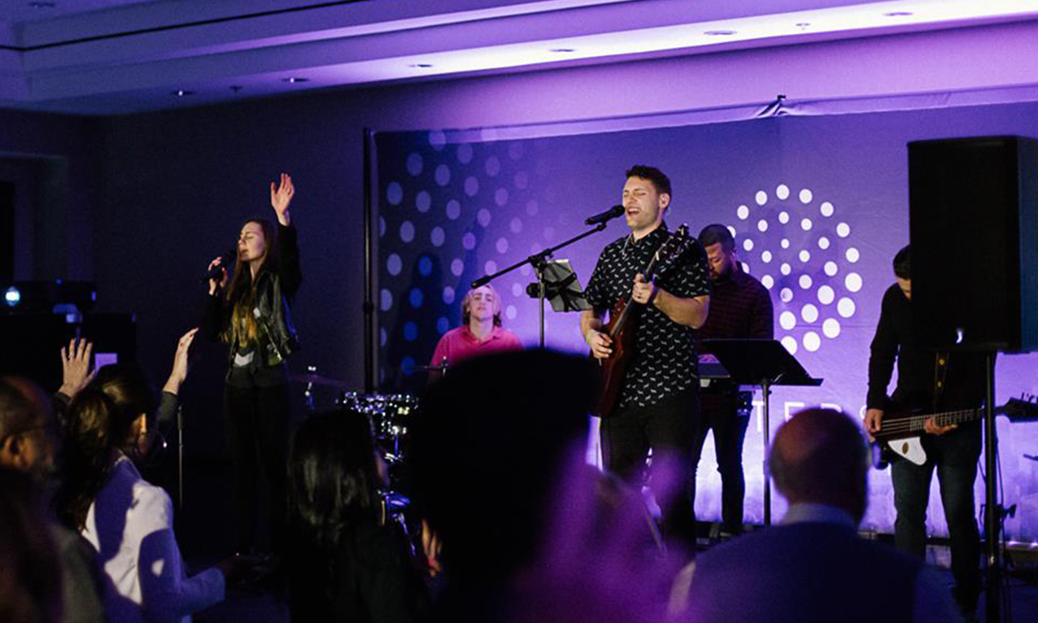 A band performing on stage with purple background lighting.