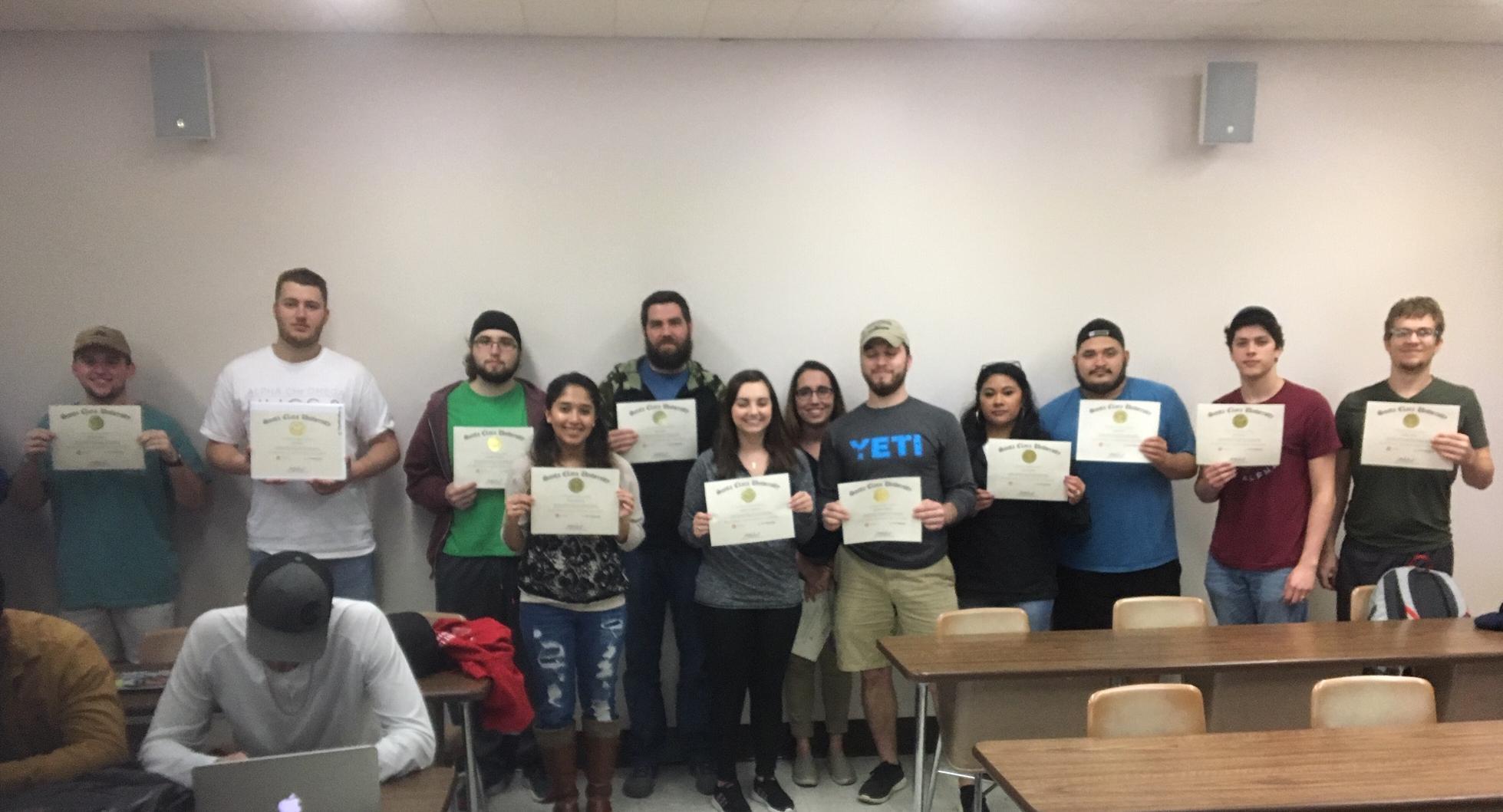 Group photo of graduates holding certificates in a classroom setting.