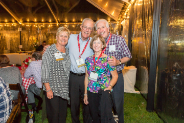 Two couples stand together and smile under a lit up tent celebrating the Class of 1965