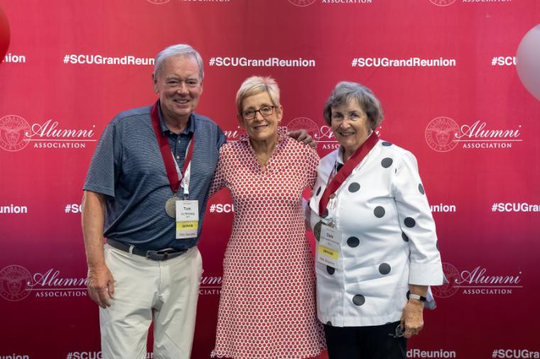 A man and woman wear their Gianera medals and stand on either side of President Julie Sullivan